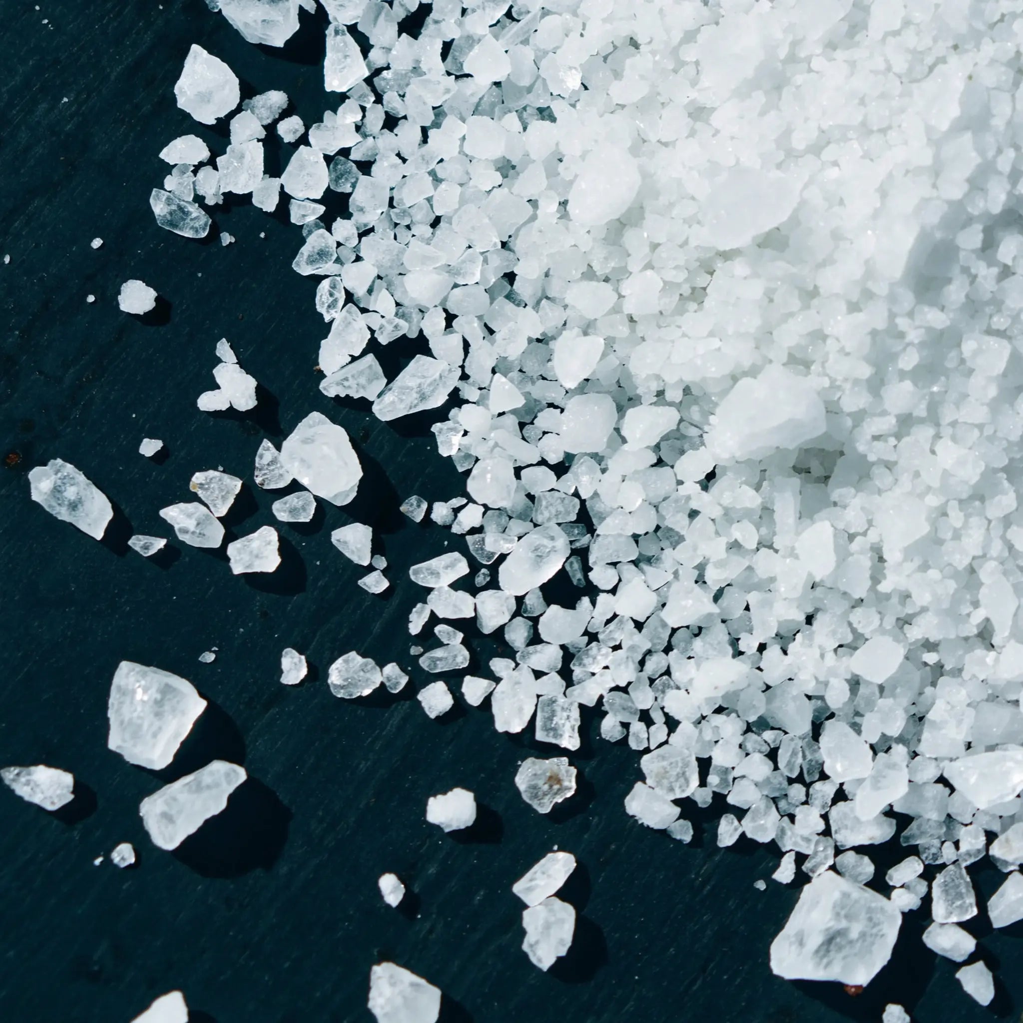 Coarse sea salt crystals and mineral electrolytes on a dark slate surface